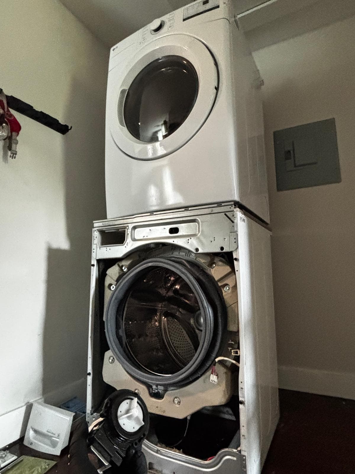 Stacked front-load washer front panel removed in Connecticut home — door boot seal and drain pump exposed for replacement